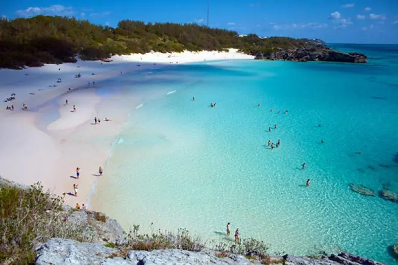 Bermuda cruise deal showcasing a ship approaching pink-sand beaches, crystal-clear waters, and pastel-colored colonial towns along the Atlantic coast