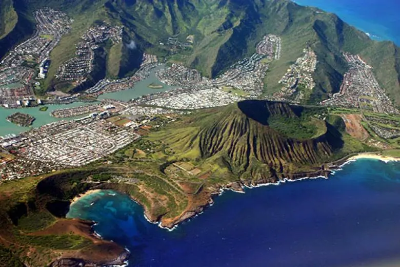 Hawaii cruise deal showcasing a ship sailing toward volcanic islands, lush green mountains, and tropical beaches across the Pacific Ocean
