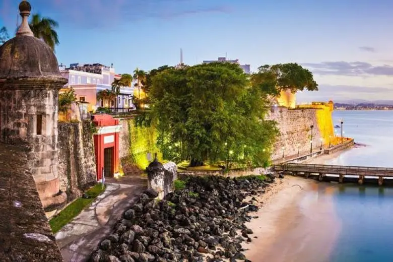 Puerto Rico cruise deal featuring a ship sailing toward San Juan with views of colorful colonial streets, historic forts, and lush tropical coastlines